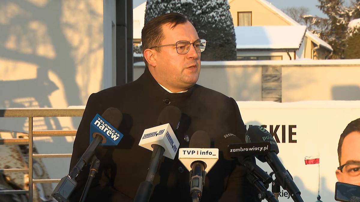 Mężczyzna w okularach przemawia do mikrofon&oacute;w.