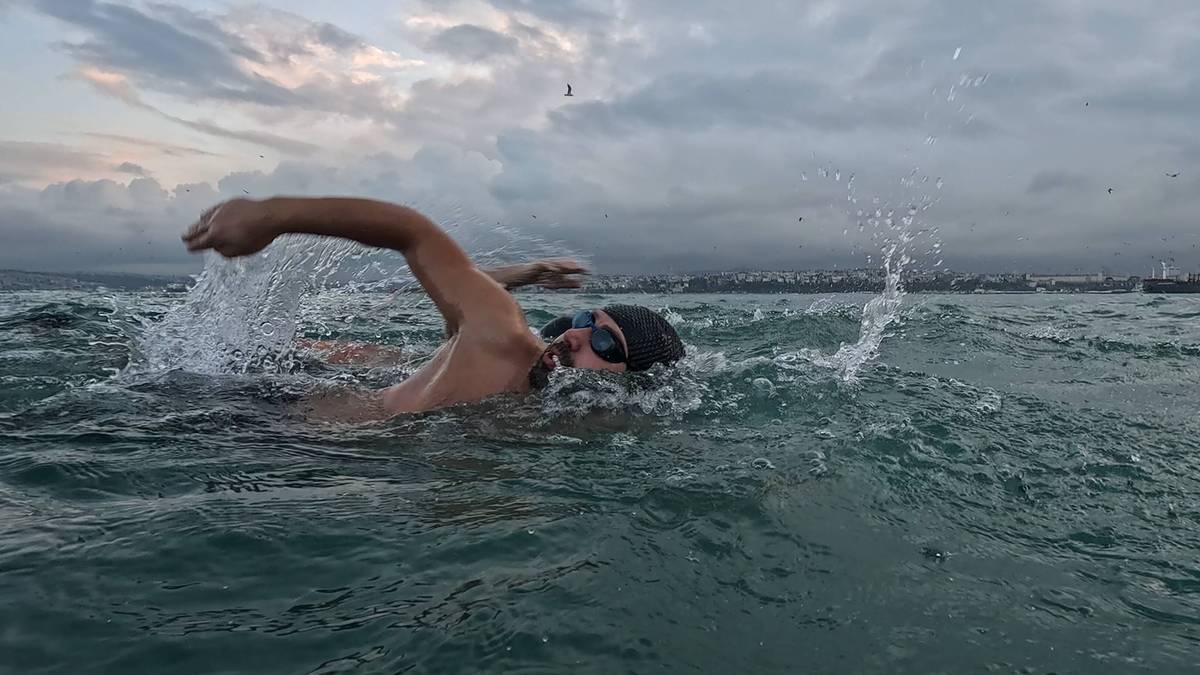 Mężczyzna w czepku pływackim i okularach pływa stylem motylkowym w oceanie.