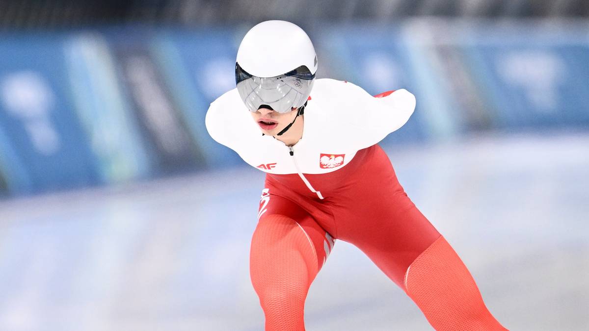 Panczenista w czerwonym stroju z białym orłem na piersi podczas biegu na lodowisku.