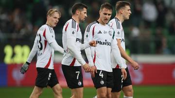 Czterech piłkarzy w białych strojach z czarnymi detalami idzie po boisku.