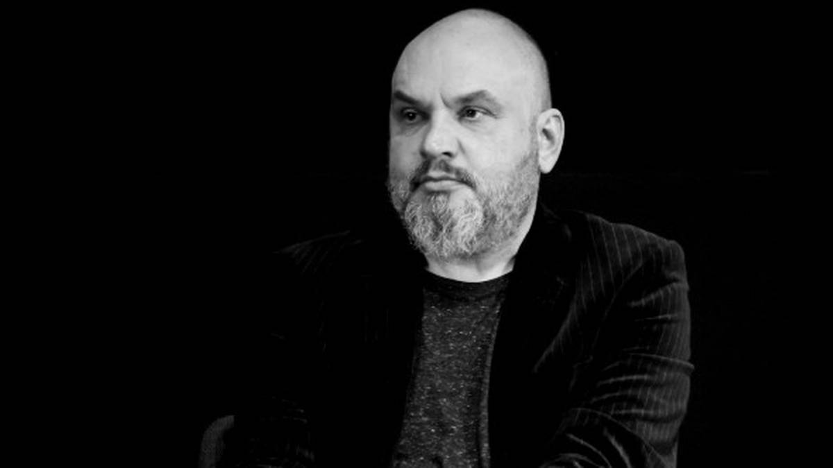 Czarno-biały portret dojrzałego mężczyzny z brodą i ogoloną głową, ubranego w marynarkę.