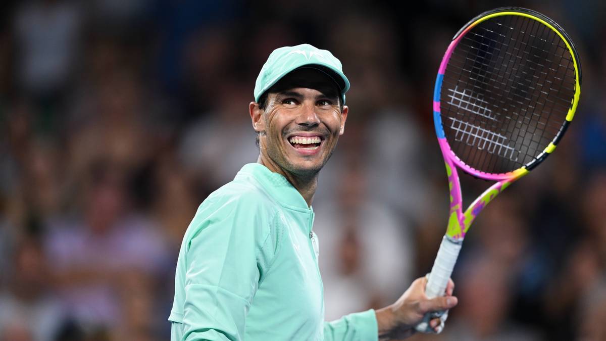 Rafael Nadal uśmiecha się trzymając rakietę tenisową.