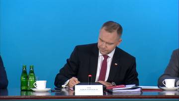 Prezydent Karol Nawrocki siedzi przy stole, pochylony nad dokumentami, podpisuje ustawę.