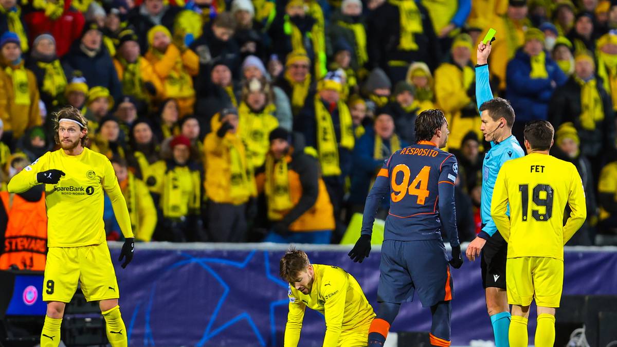 Piłkarze rywalizujący na boisku, sędzia pokazujący ż&oacute;łtą kartkę jednemu z zawodnik&oacute;w.