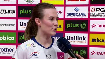 Piłkarka ręczna Justyna Łysiak, ubrana w biało-niebieski str&oacute;j sportowy z numerem 10, udziela wywiadu przed ścianką sponsorską.