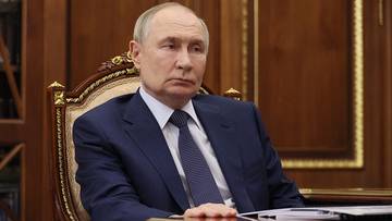 Władimir Putin siedzi przy biurku w eleganckim wnętrzu.