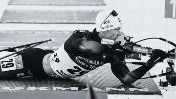 Biathlonista w pozycji leżącej celuje z karabinu na strzelnicy.