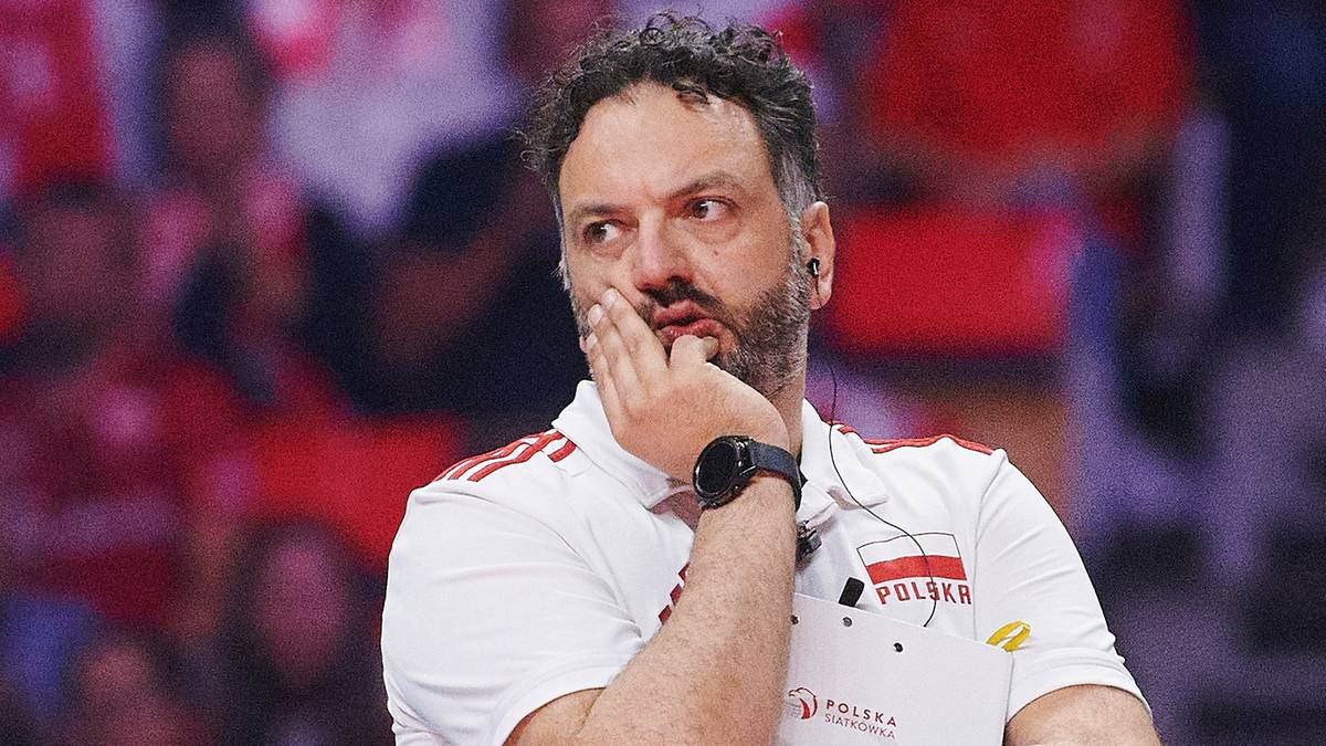 Portret Stefano Lavariniego, trenera siatkówki, w białej koszulce z godłem Polski. Lavarini przytrzymuje dłoń przy policzku, patrząc w bok z zamyślonym wyrazem twarzy.