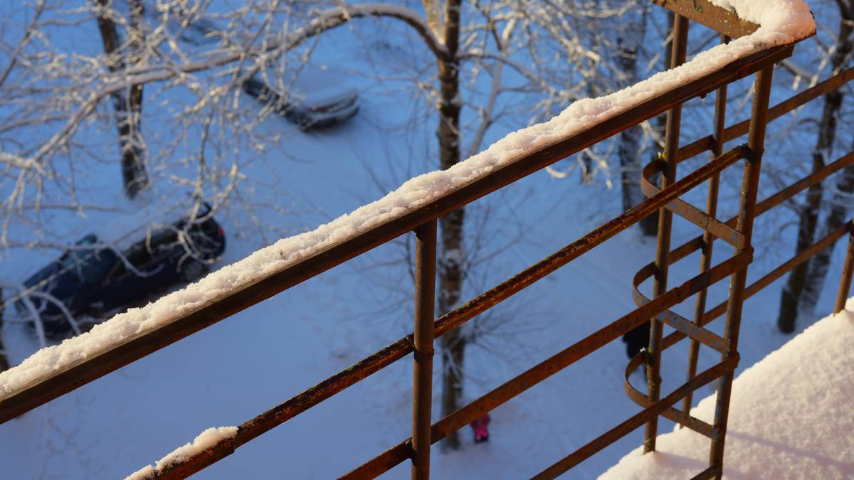 Zimowy widok na balkon pokryty śniegiem i ośnieżone drzewa w tle.