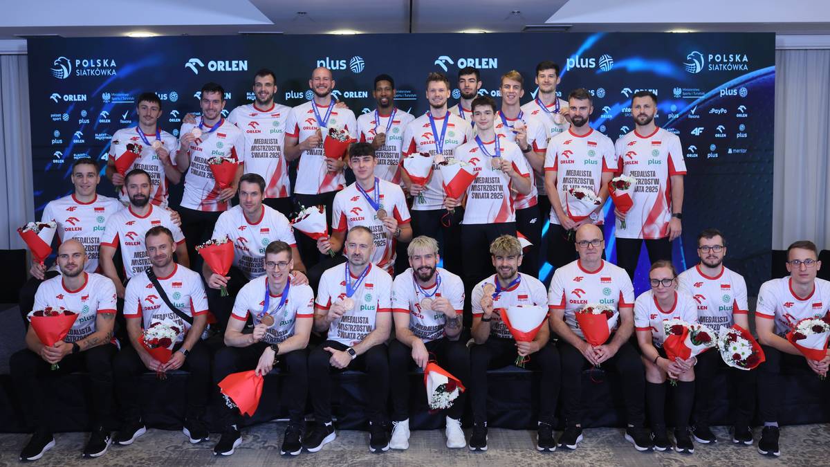 Drużyna siatkarzy w czerwonych koszulkach stoi w rzędzie, pozując do zdjęcia. Na ich twarzach widać uśmiechy i radość.