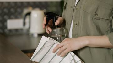 Osoba trzyma butelkę z rozpylaczem i ściereczkę, przygotowując się do sprzątania.