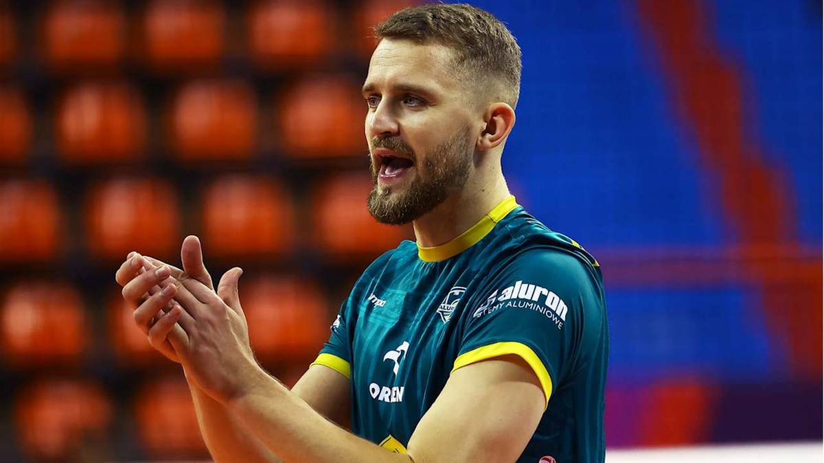 Mężczyzna w zielono-ż&oacute;łtej koszulce siatkarskiej, ze zmarszczonymi brwiami i otwartymi ustami, gestykuluje obiema rękami, jakby dawał wskaz&oacute;wki.