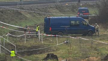 Niebieski van policyjny i inni funkcjonariusze na miejscu zdarzenia otoczonym taśmą, w pobliżu torów kolejowych.