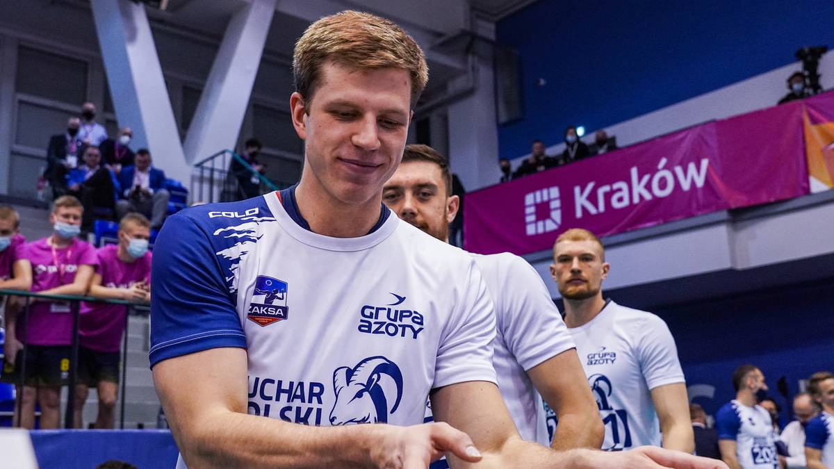 Siatkarz w białej koszulce z niebieskimi akcentami, skupiony na grze podczas meczu.