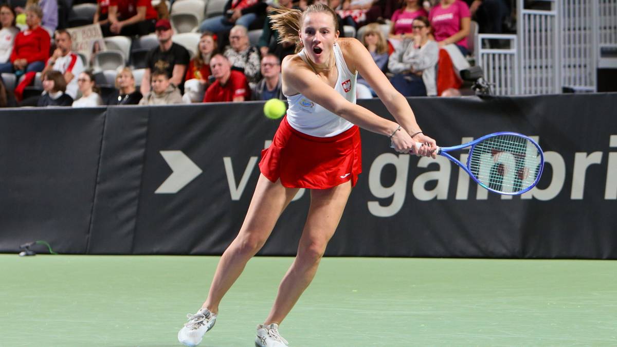 Tenisistka wykonuje forhendowy wolej na korcie tenisowym, w tle publiczność.