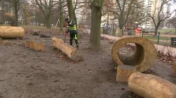 Osoba w kamizelce odblaskowej pracuje przy budowie placu zabaw z naturalnych elementów, takich jak pnie drzew i drewniane kłody.