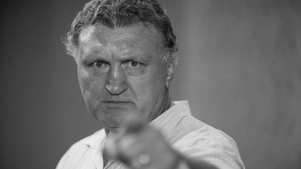 Czarno-białe zdjęcie starszego mężczyzny z surowym wyrazem twarzy, który wskazuje palcem w stronę widza.