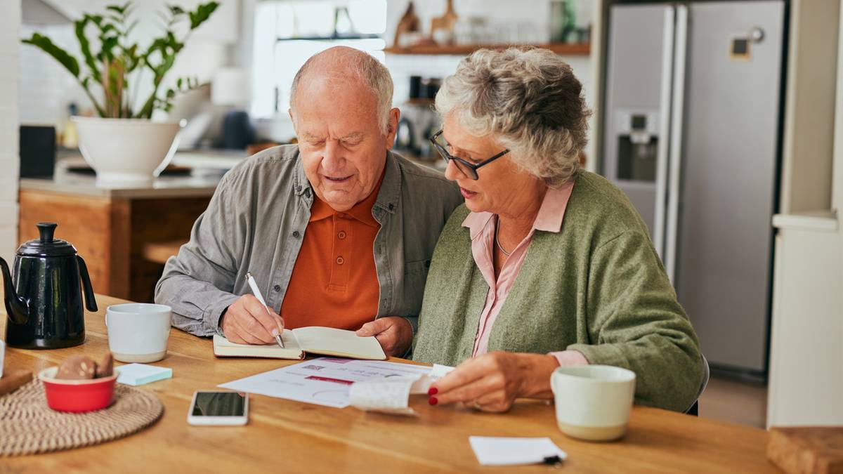 Starsza para przy stole przegląda dokumenty i pisze w notatniku.
