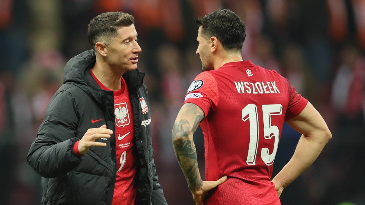 Dwóch piłkarzy reprezentacji Polski w czerwonych strojach rozmawia na boisku.