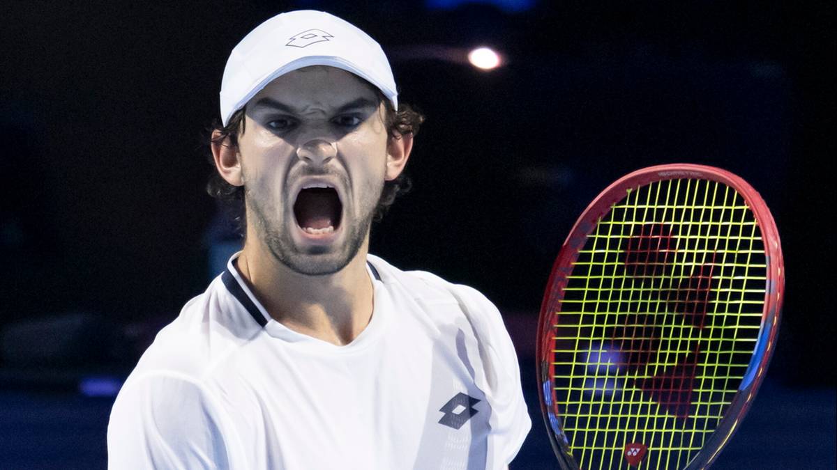 Tenisista w białej czapce i koszulce z otwartymi ustami, trzymający rakietę tenisową.