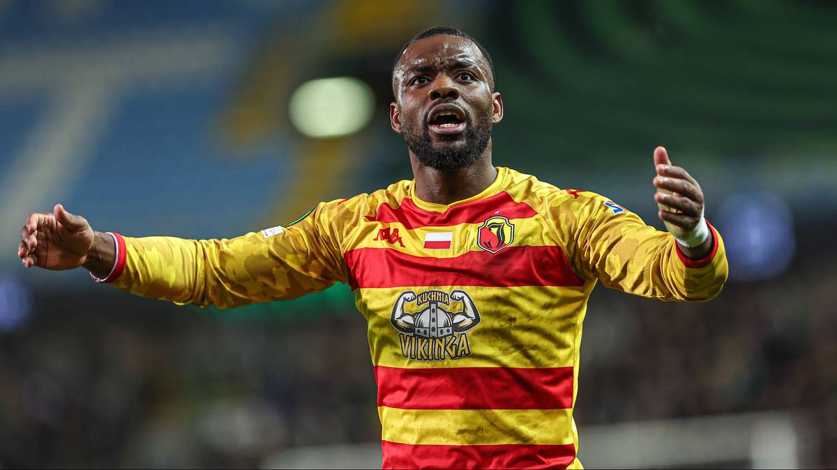 Piłkarz w żółto-czerwonej koszulce strzela bramkę, koncentrując się na grze.