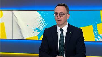 Mężczyzna w garniturze i okularach z krawatem siedzi i m&oacute;wi.