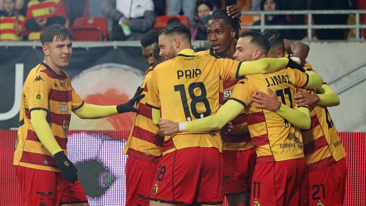 Drużyna piłkarska Jagiellonii Białystok w żółto-czerwonych strojach świętuje razem na boisku.