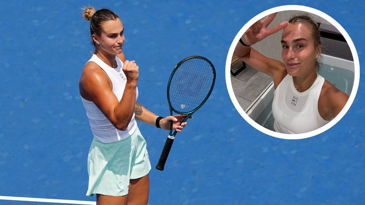 Aryna Sabalenka w białej koszulce i jasnych spodenkach, trzymająca rakietę tenisową w prawej dłoni, z uniesionym lewym pięścią, na niebieskim tle kortu tenisowego.