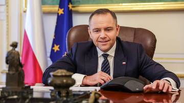 Prezydent Karol Nawrocki siedzi przy biurku, za nim widoczne flagi Polski i UE.