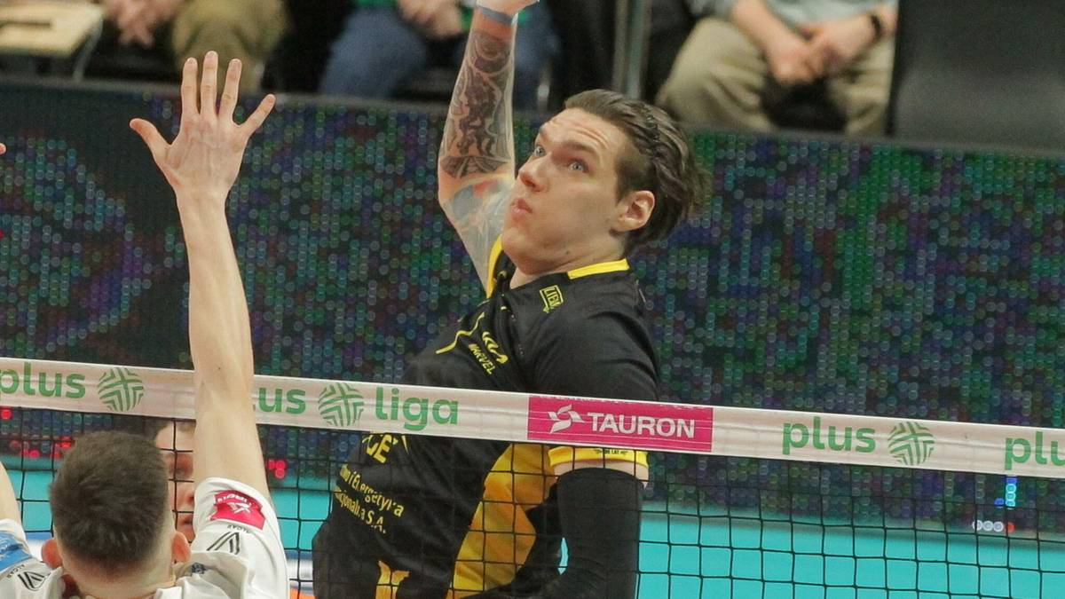 Siatkarz w czarno-ż&oacute;łtym stroju atakuje piłkę nad siatką, podczas gdy drugi zawodnik w białym stroju pr&oacute;buje ją zablokować.