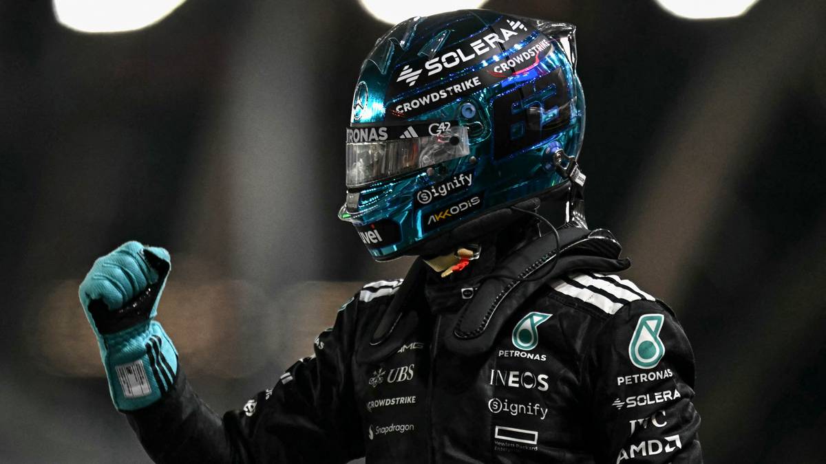 Kierowca Formuły 1 w kasku z niebieskimi elementami i logo zespołu Mercedes-AMG Petronas, unosi zaciśniętą pięść w geście triumfu. Widoczny fragment kombinezonu wyścigowego.
