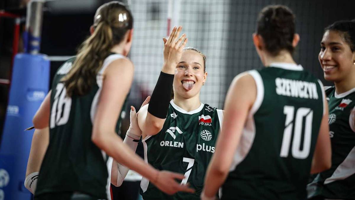 Cztery zawodniczki siatkówki w zielonych strojach z białymi detalami, stoją blisko siebie,ungaśmiejąc się i ciesząc. Jedna z nich, numer 7, wystawia język.