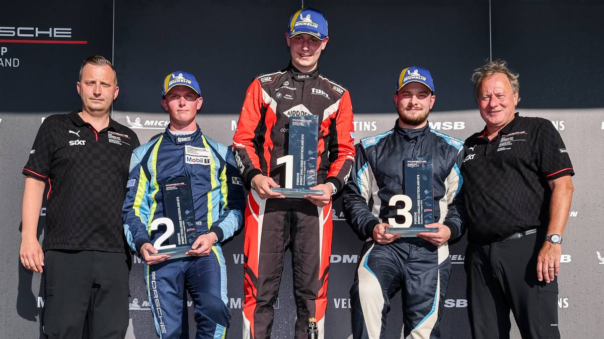 Trzech młodych kierowców, zwycięzców zawodów sportów motorowych, stoi na podium. Dwóch starszych mężczyzn stoi po bokach, po jednym z każdej strony, trzymając trofea.