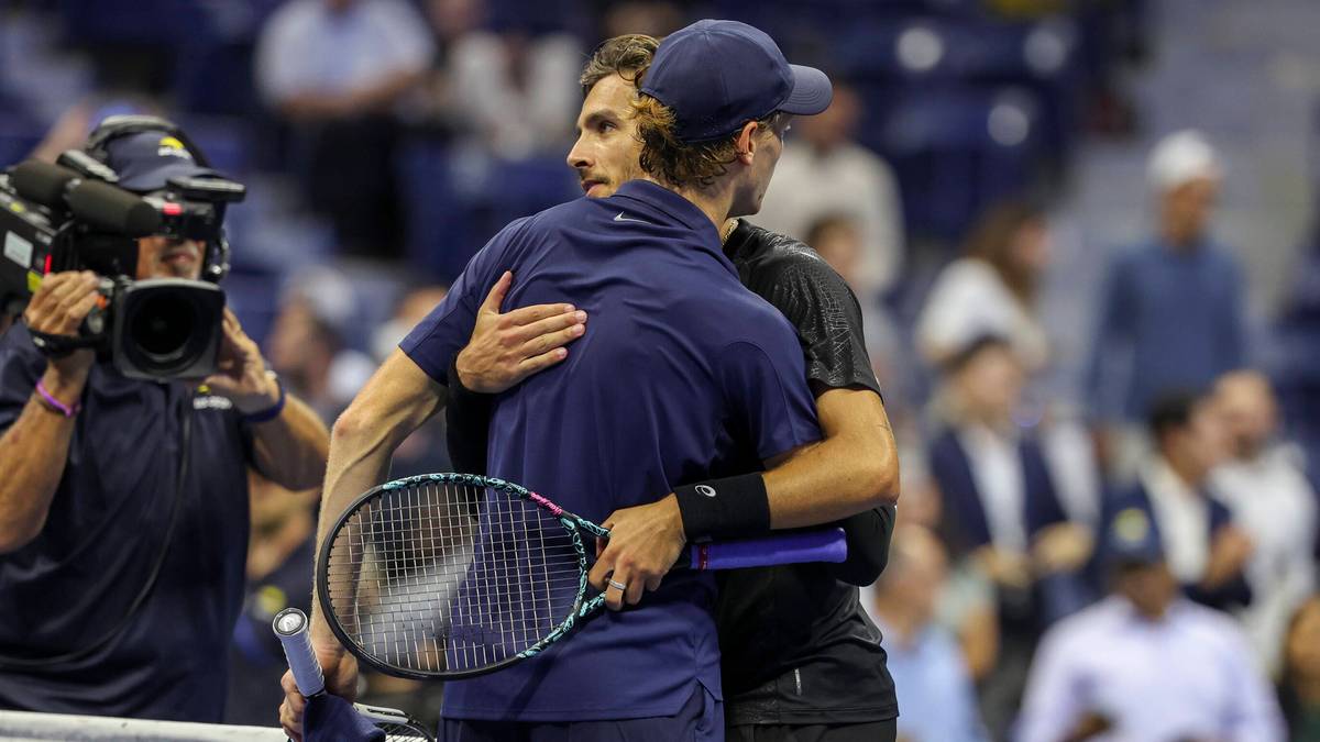 Dwóch mężczyzn w strojach tenisowych przytula się na korcie tenisowym, jeden z nich trzyma rakietę.