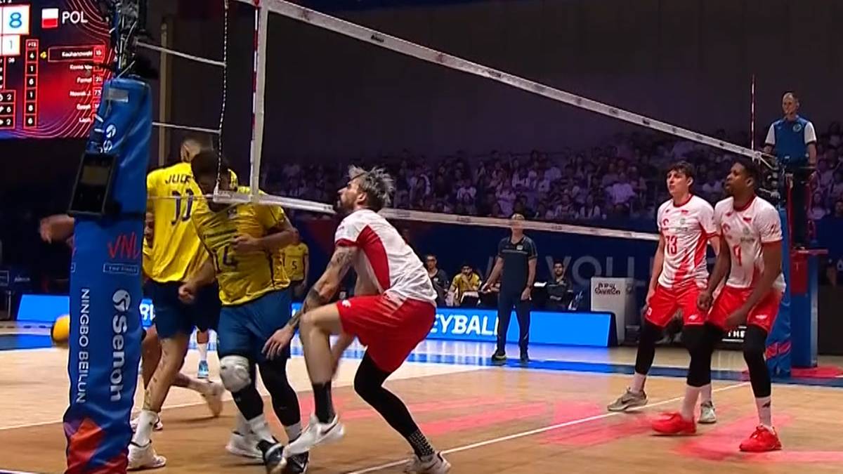 Siatkarz w żółtej koszulce upada na boisko podczas meczu, podczas gdy inni zawodnicy w białych koszulkach próbują interweniować.