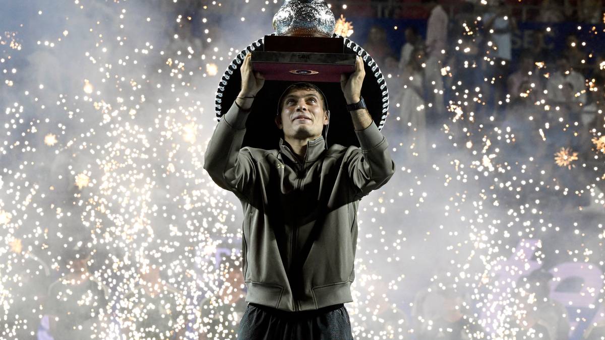 Tenisista Flavio Cobolli trzyma puchar nad głową na tle fajerwerk&oacute;w.