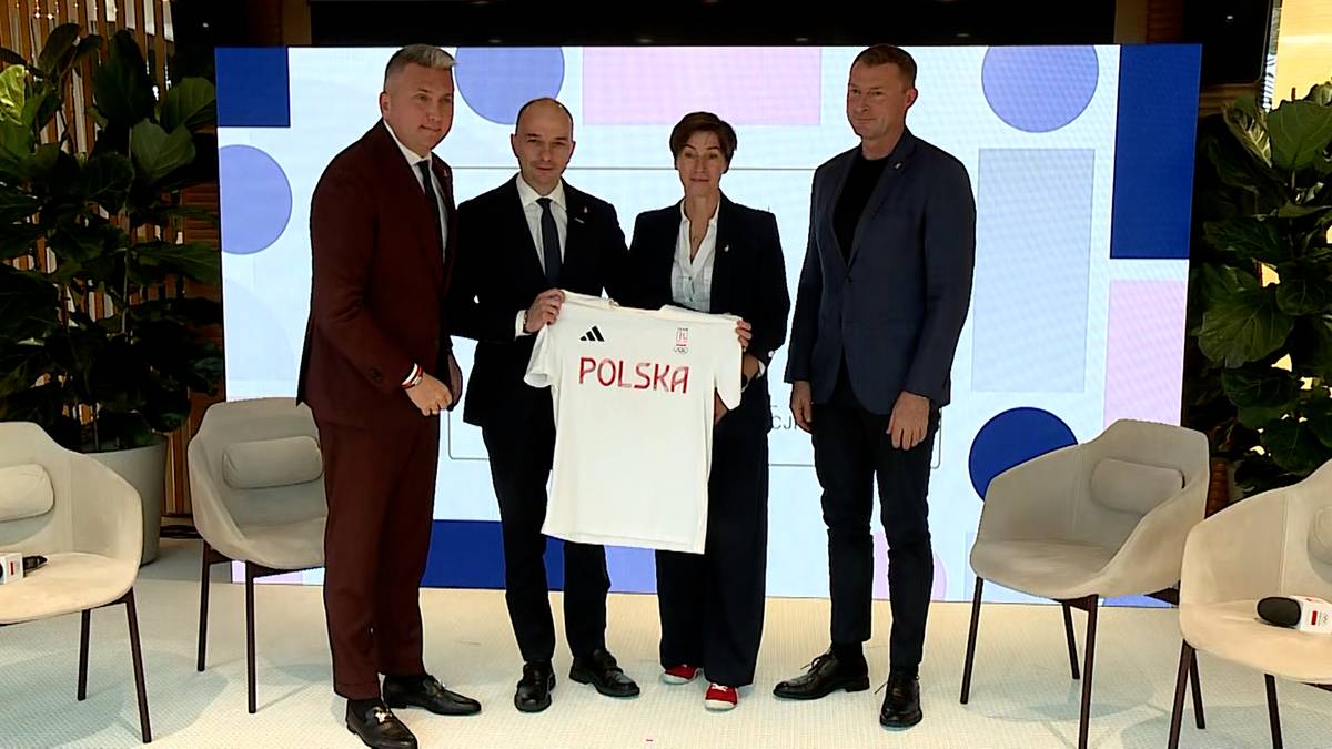 Cztery osoby stojące obok siebie, z których dwie środkowe trzymają białą koszulkę piłkarską z napisem "POLSKA".