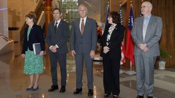 Grupa pięciu os&oacute;b, w tym cztery kobiety i jeden mężczyzna, stoi w pomieszczeniu z flagami USA i Tajwanu w tle. Wszyscy ubrani są formalnie.