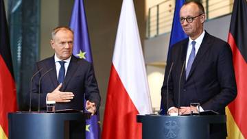 Dwóch mężczyzn w garniturach stoi za mównicami, z flagami Polski i Niemiec w tle.