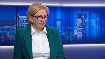 Joanna Wicha, polityczka Lewicy, w białej koszuli i zielonej marynarce, patrzy w bok z lekkim uśmiechem. W tle widać niebieskie ekrany z widokiem nocnego miasta.