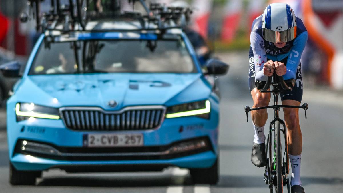 Kolarz w niebieskim stroju z białym kaskiem ściga się na rowerze obok niebieskiego samochodu.