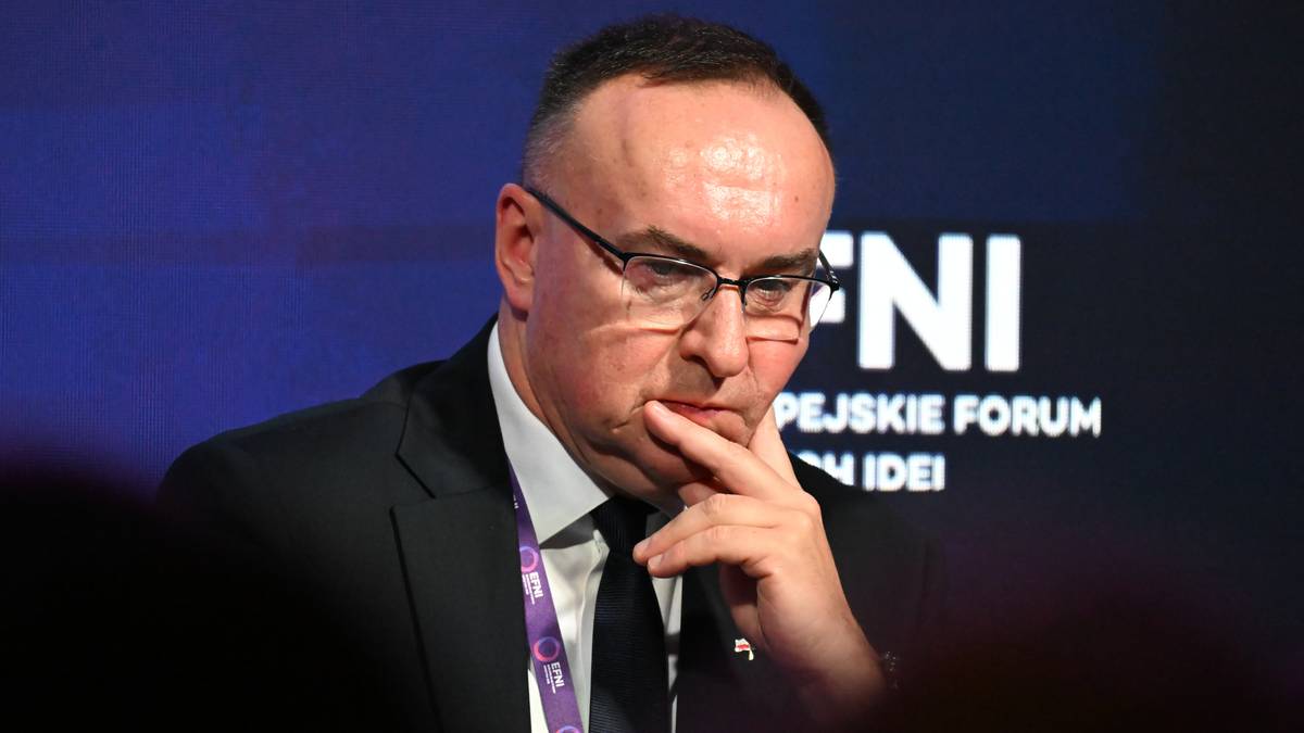 Michał Kobosko w okularach, w garniturze, z dłonią na brodzie.