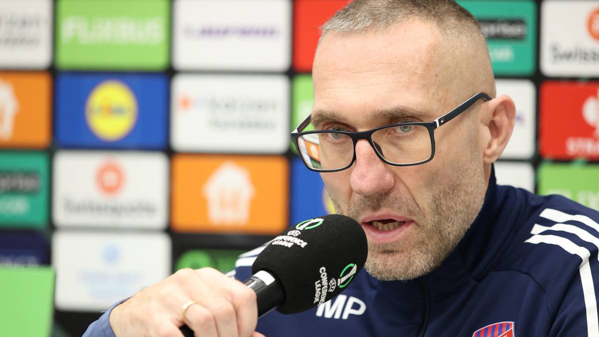 Mężczyzna w okularach i sportowej kurtce z mikrofonem przed ustami.