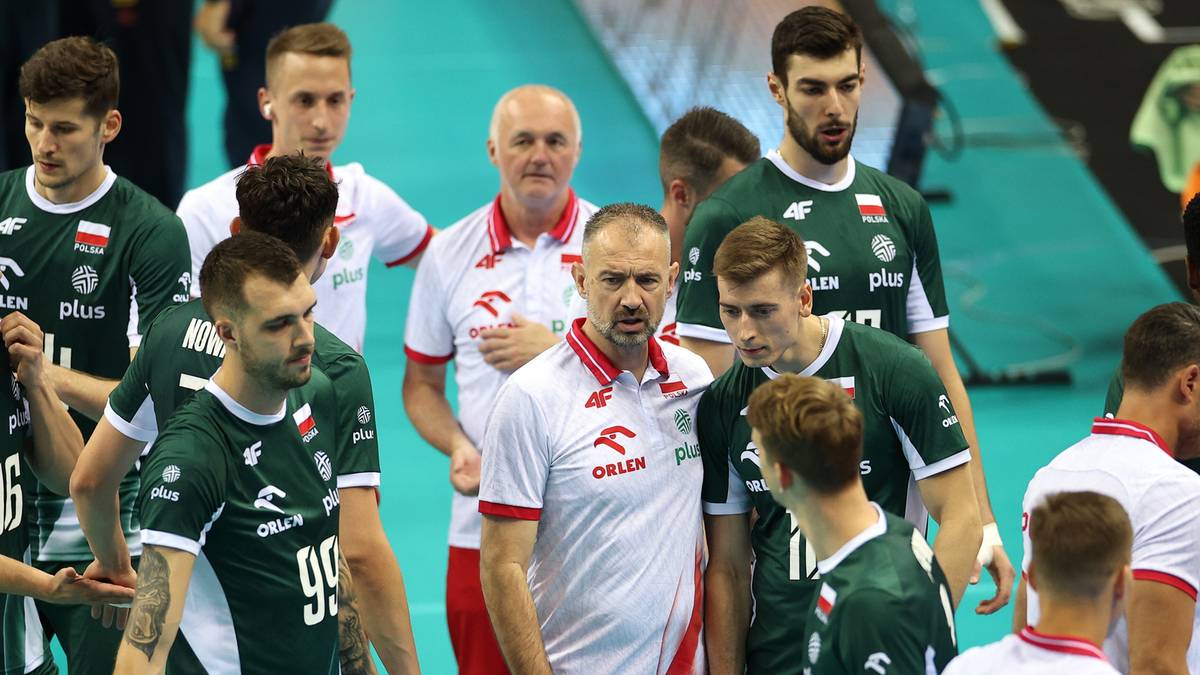 Grupa męskiej drużyny siatkarskiej w zielonych strojach sportowych z białymi elementami, stoi razem patrząc w prz&oacute;d. Widoczni są r&oacute;wnież trenerzy w białych koszulkach.