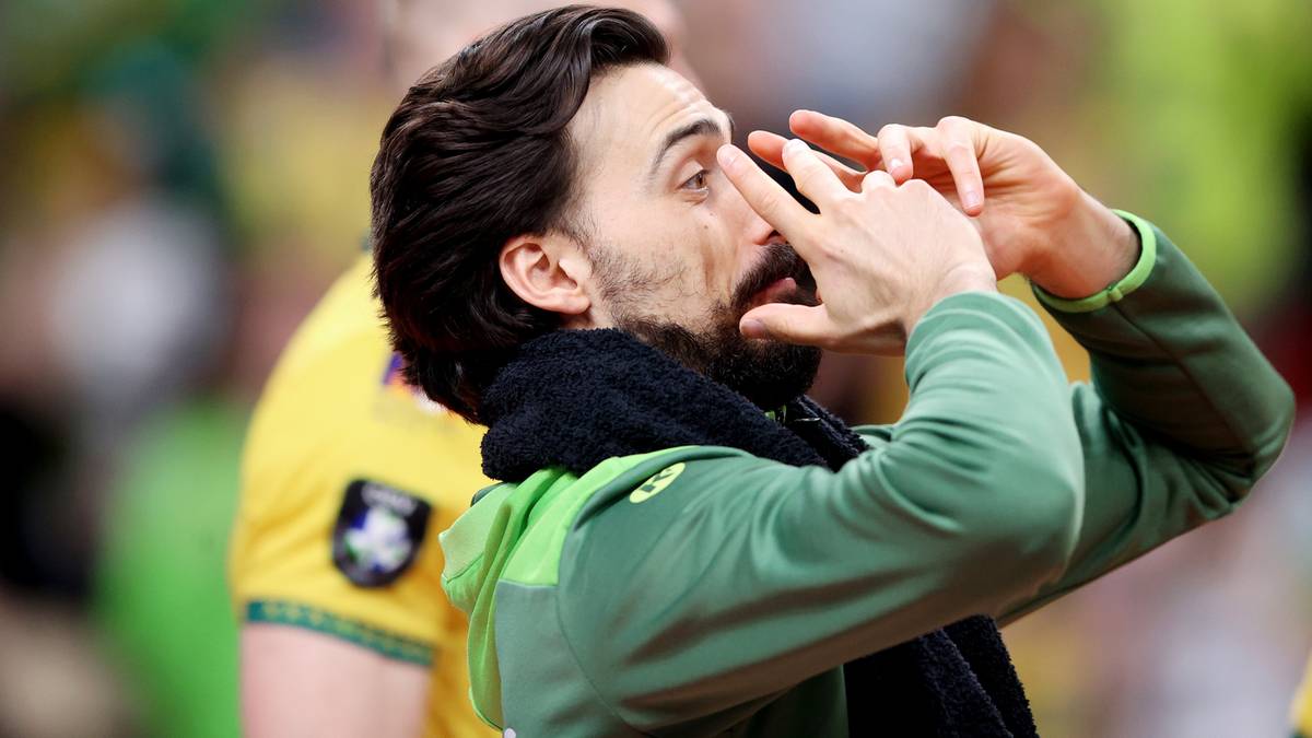 Mężczyzna w bluzie krzyczy z rękami przy twarzy.