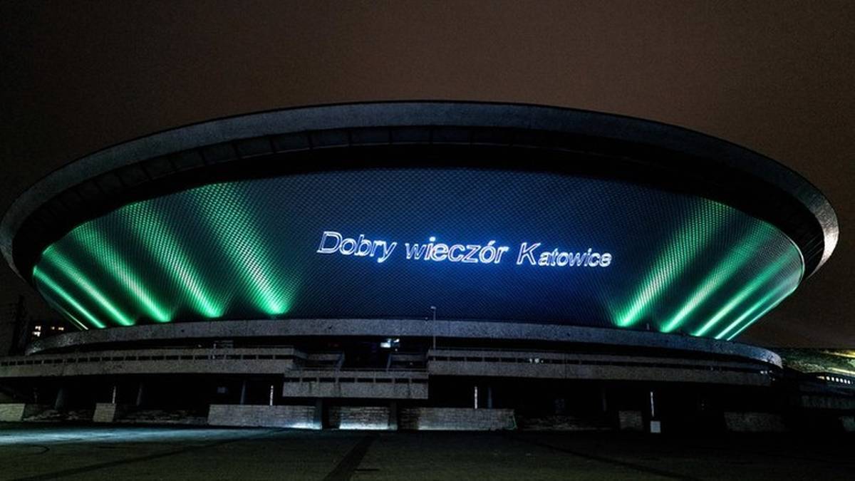 Nocny widok na katowicki Spodek z napisem "Dobry wieczór Katowice" i zielonymi światłami.