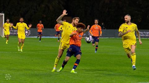 Dw&oacute;ch piłkarzy w ż&oacute;łtych strojach rywalizuje o piłkę na boisku piłkarskim, z innymi graczami w tle.