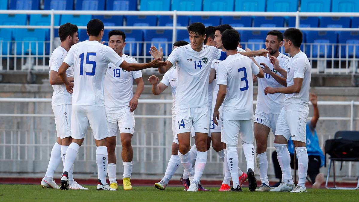 Grupa piłkarzy w białych strojach grających w piłkę nożną, świętujących razem na boisku stadionu.