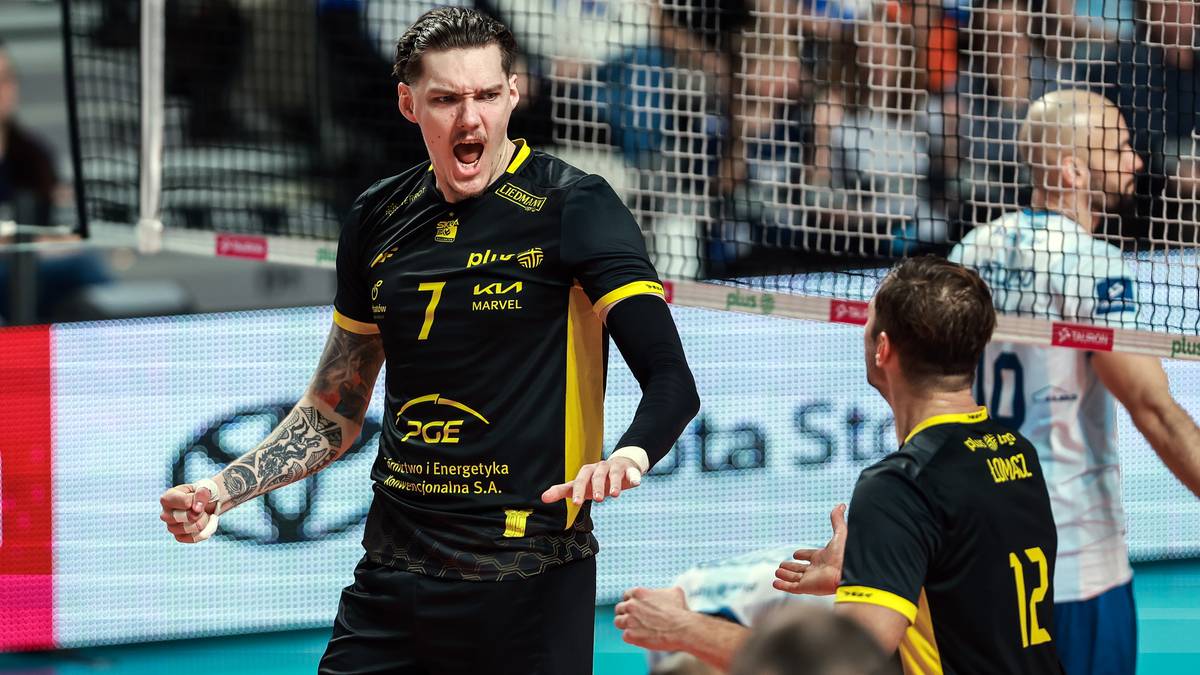 Siatkarz w czarno-ż&oacute;łtej koszulce z numerem 7 krzyczy z radości, patrząc w bok, z innymi graczami w tle.