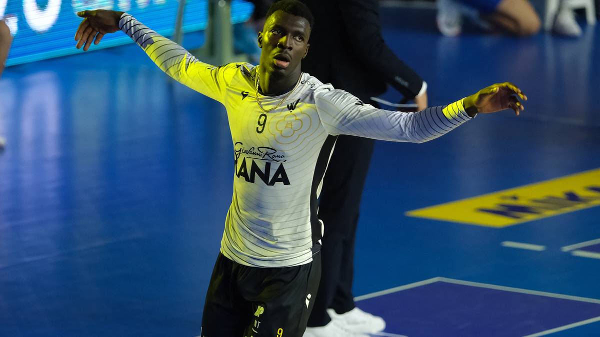 Siatkarz w białej koszulce z numerem 9 i czarnych spodenkach wykonuje ruch rękami na parkiecie.